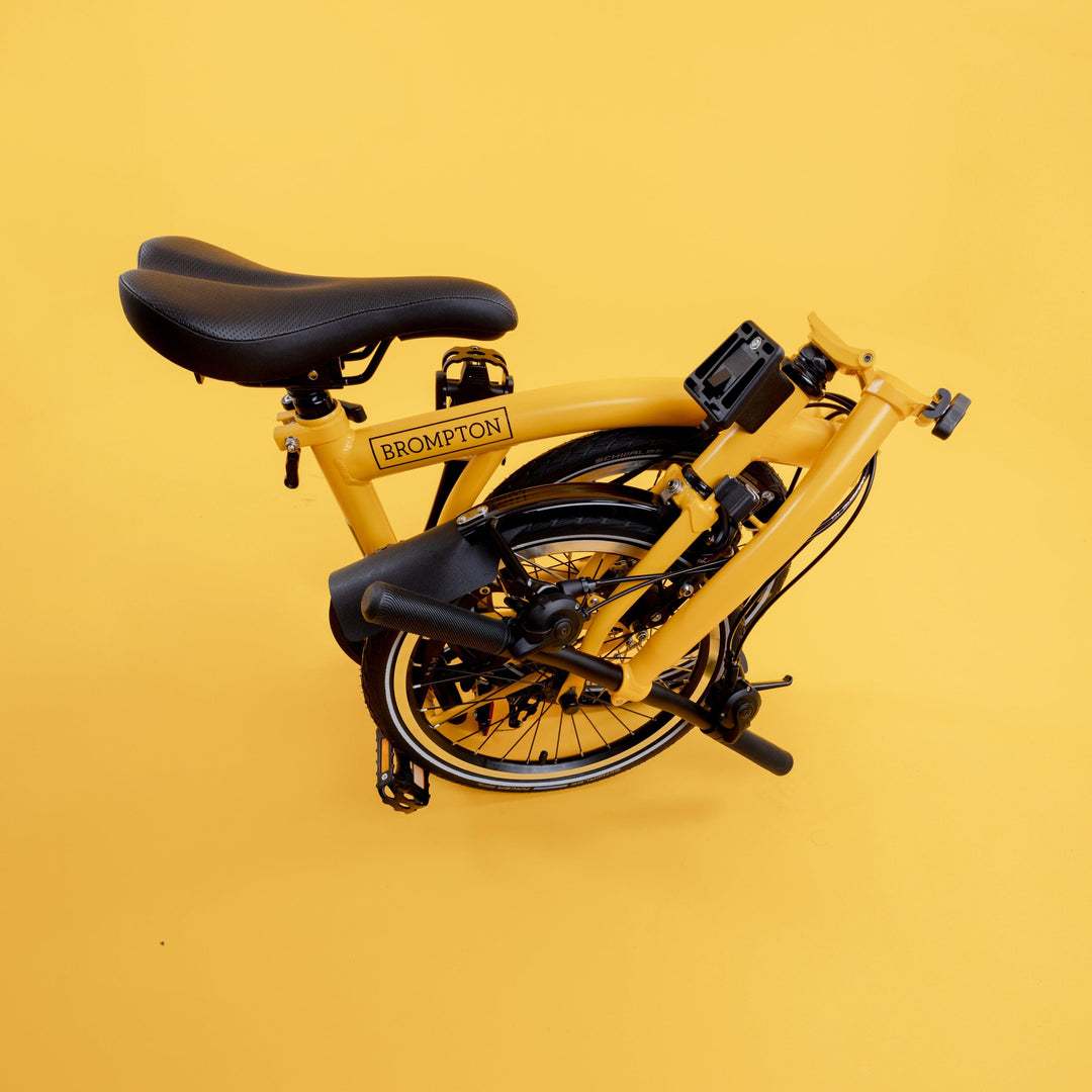 Folded British Brompton C Line Bike in Bumblebee Yellow with Low Handlebar on Yellow Background